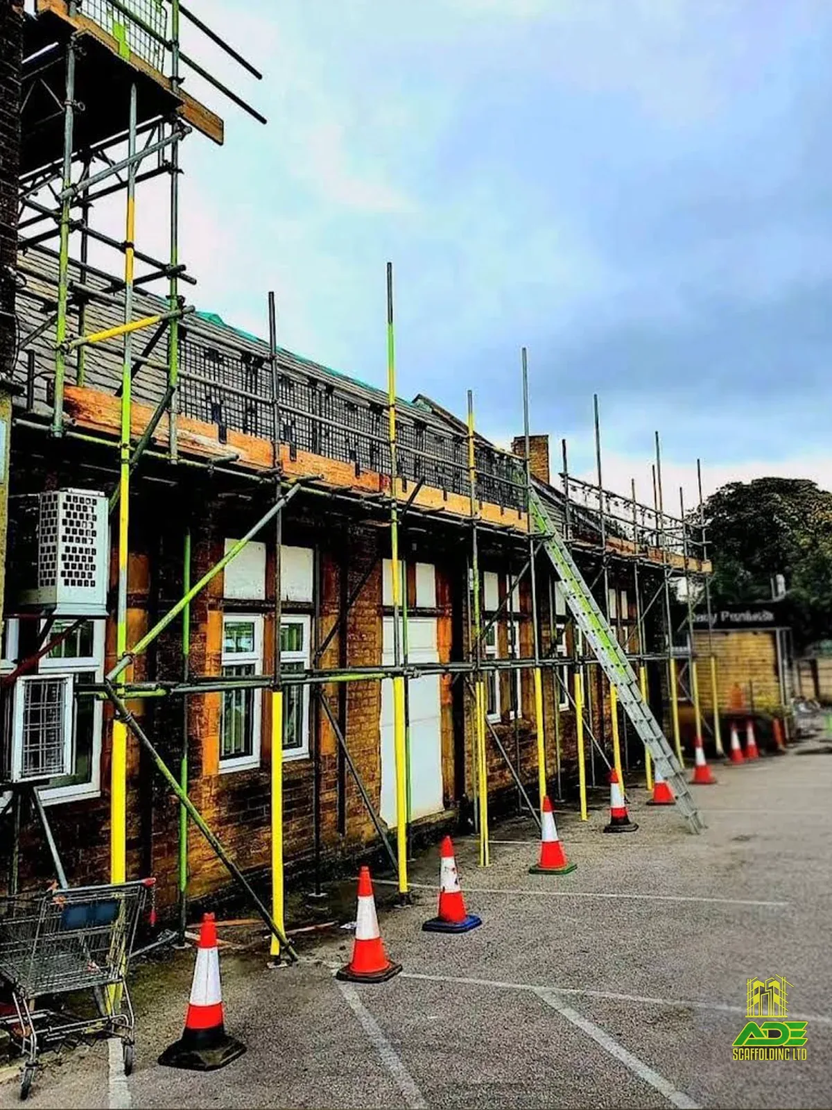 Pavement scaffold along a brick commercial building with cones and ladder